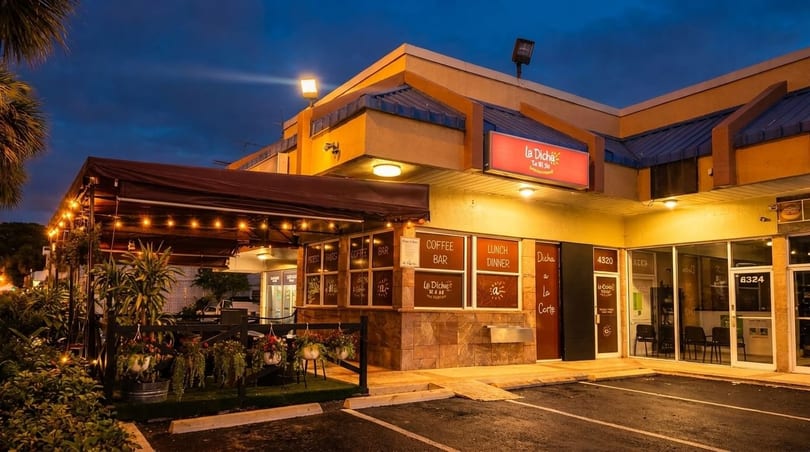 Exterior of La Dicha restaurant at dusk, with an illuminated patio and string lights.
