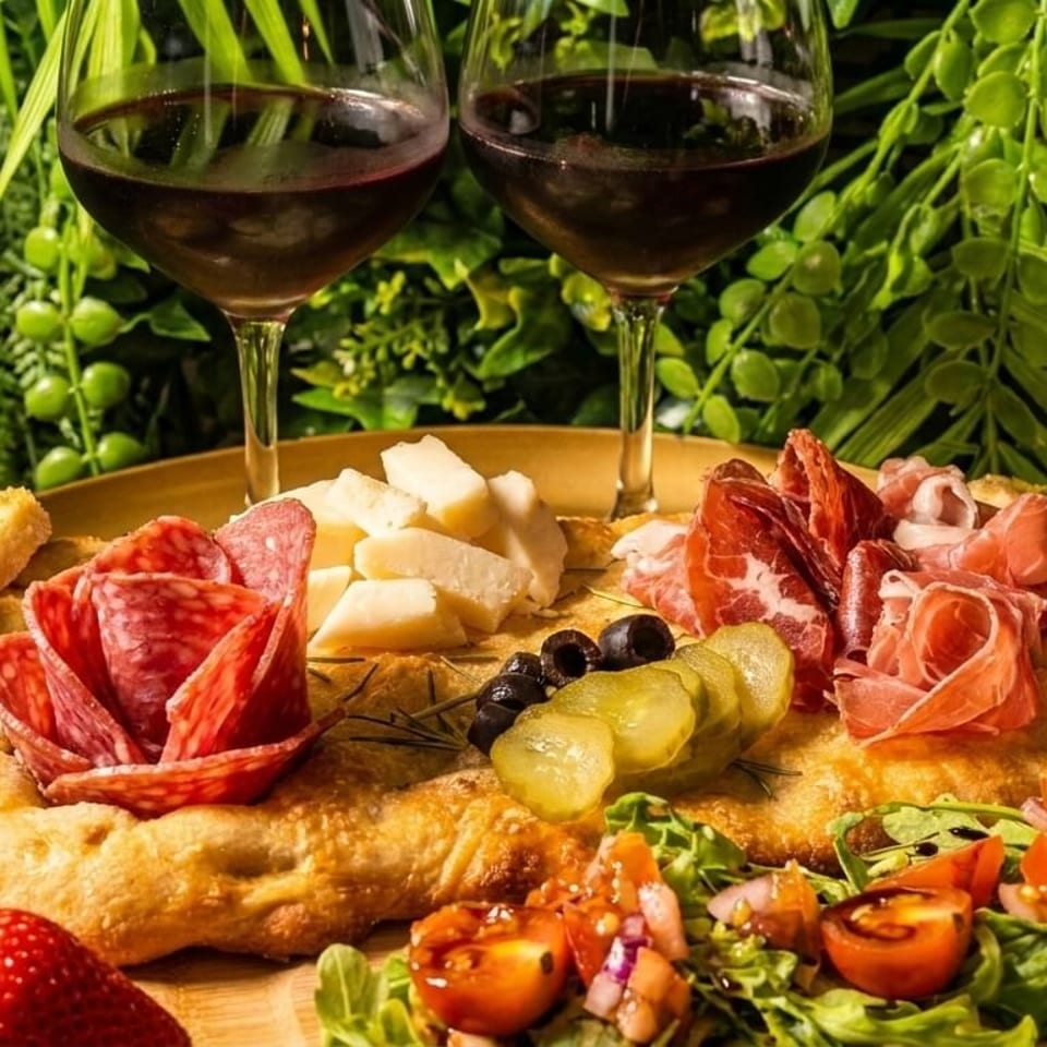 Two glasses of red wine with a charcuterie board featuring meats, cheeses, olives, and bruschetta.