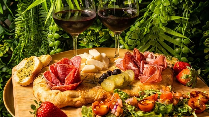 Two glasses of red wine with a charcuterie board featuring meats, cheeses, olives, and bruschetta.