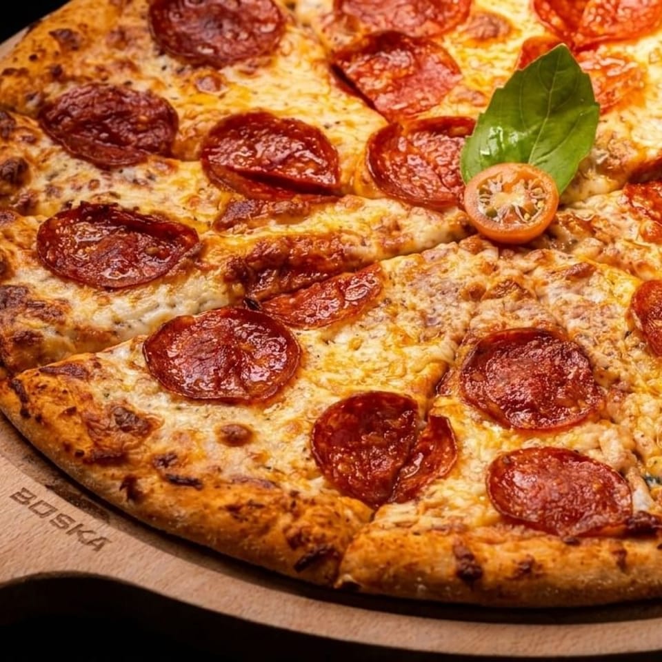 Pepperoni pizza with basil and cherry tomato on a wooden serving board.