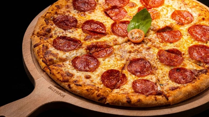 Pepperoni pizza with basil and cherry tomato on a wooden serving board.