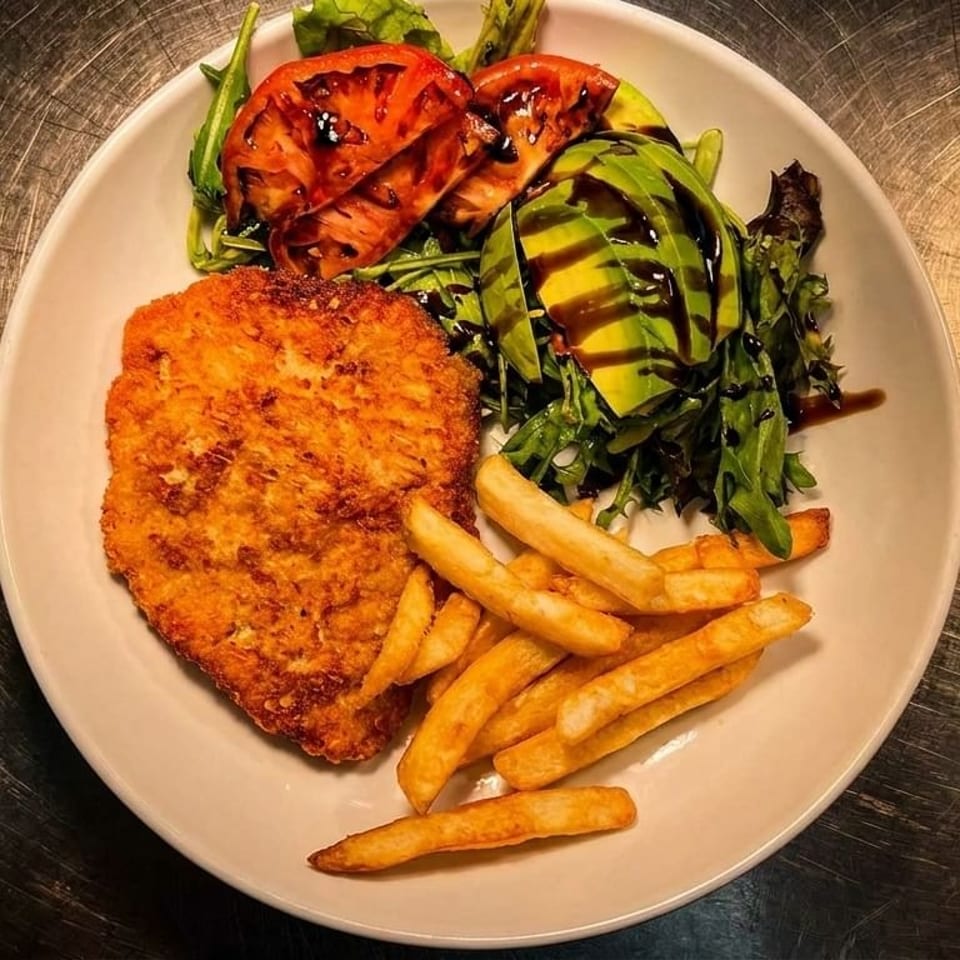 Crispy fried chicken schnitzel with golden fries, avocado, grilled tomatoes, and a green salad.