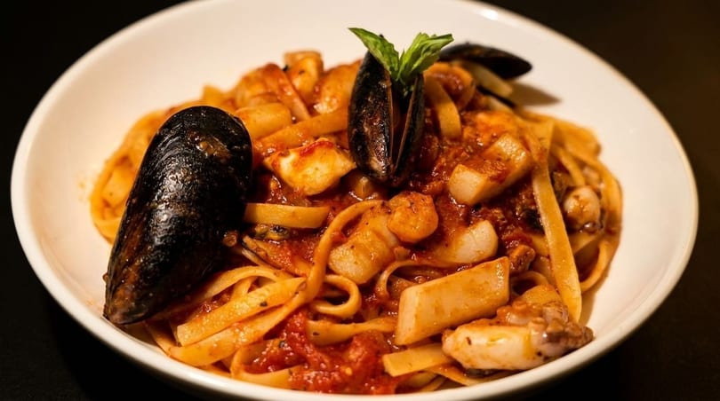 Seafood linguine with mussels, calamari, and scallops in a rich red sauce, garnished with basil.