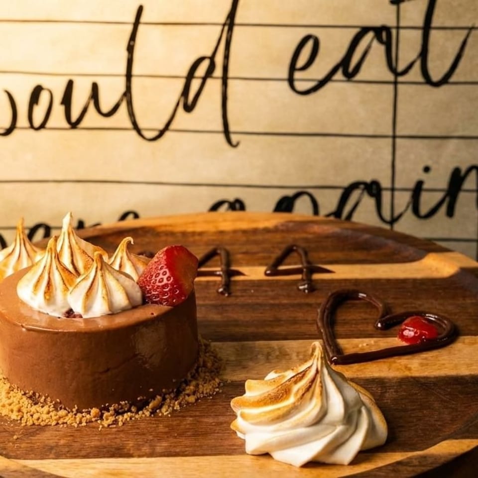 Chocolate dessert with meringue, strawberry, and chocolate sauce on a wooden board.