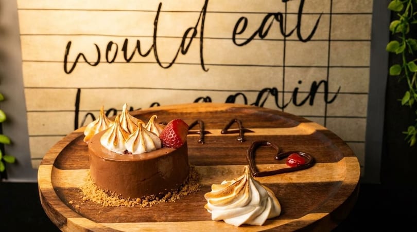 Chocolate dessert with meringue, strawberry, and chocolate sauce on a wooden board.