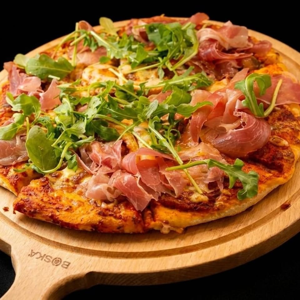 A delicious pizza topped with prosciutto and fresh arugula, served on a wooden pizza peel.
