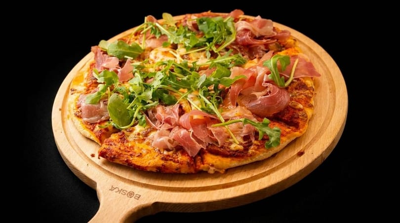A delicious pizza topped with prosciutto and fresh arugula, served on a wooden pizza peel.